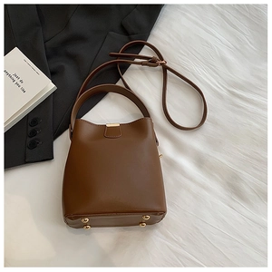 Detail view of brown bucket bag showing adjustable strap and protective metal feet