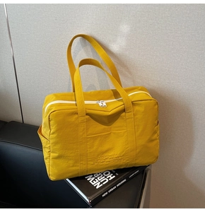 Detail of yellow nylon tote bag featuring durable white dual zippers and side pocket on sofa