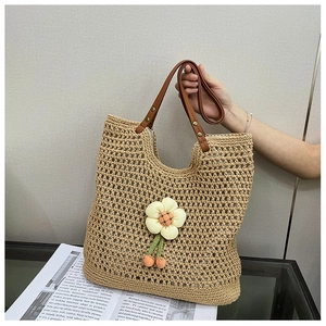 Dettaglio della borsa tote in paglia intrecciata con manico in pelle e ciondolo
