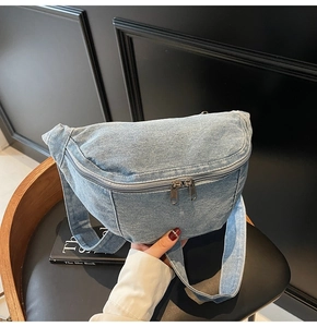 Detail of light blue washed denim chest bag with vintage texture and silver zippers