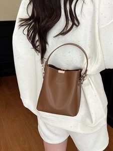 Brown leather bucket bag with top handle and shoulder strap shown on a female model