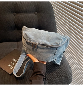 Close-up of light blue denim chest bag showing metal double zippers on corduroy chair