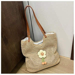 Dettaglio della borsa tote intrecciata con ciondolo a girasole e manici in pelle marrone