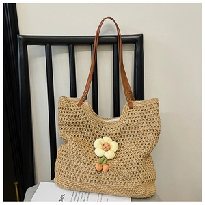 Dettaglio della borsa tote in paglia intrecciata a mano con manici in pelle e ciondolo a fiore