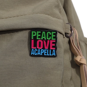 Detail of square enamel pin with colorful text on a green canvas backpack background