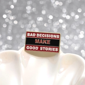 Enamel brooch with BAD DECISIONS MAKE GOOD STORIES quote in red and black