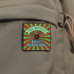 Detailed view of Fred Weasley's Basic Blaze Box enamel pin on khaki canvas fabric