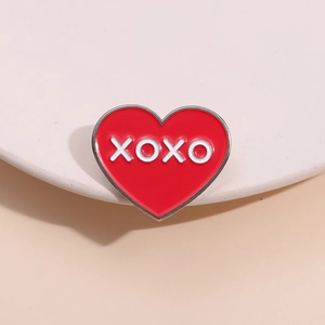 Spilla a cuore in smalto rosso con scritta XOXO bianca su un espositore elegante