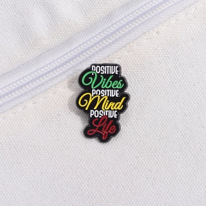 Detail of a colorful enamel positive vibes brooch on white canvas fabric background