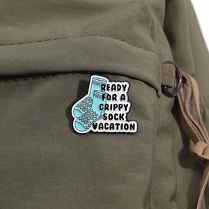 Close-up of enamel pin with grippy sock design pinned on an olive green canvas bag