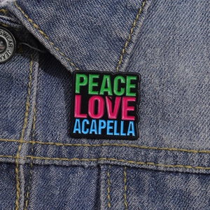 Colorful Peace Love Acapella enamel pin badge on blue denim jacket pocket detail