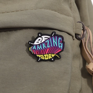 Macro detail of 'BE AMAZING TODAY' colorful enamel pin on olive green canvas fabric