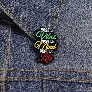 Detailed close-up of colorful Positive Vibes Mind Life enamel pin on blue denim fabric