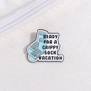 Close-up of enamel pin featuring blue socks with ready for a grippy sock vacation text