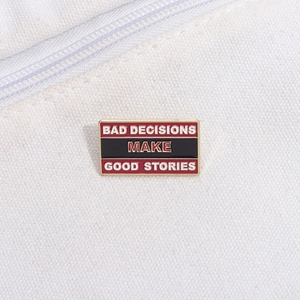 Detail of metal enamel pin badge with 'Bad Decisions Make Good Stories' text on white canvas