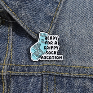 Close-up of blue grippy sock enamel pin with motivational quote on denim jacket collar