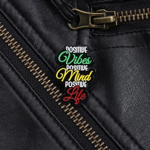 Detail of POSITIVE Vibes Mind Life enamel pin on a black leather jacket texture