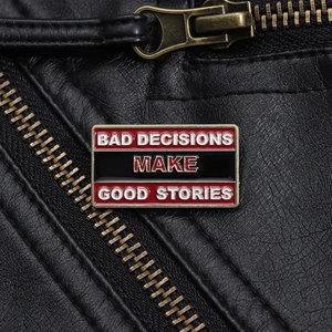 Macro shot of rectangular enamel pin with Bad Decisions Make Good Stories slogan on leather