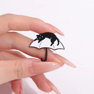 Creative black cat on white umbrella enamel pin badge held by fingers for size reference