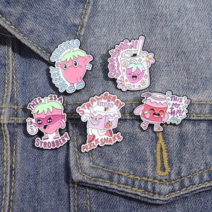Five strawberry enamel pins set on blue denim jacket pocket featuring cute cartoon designs