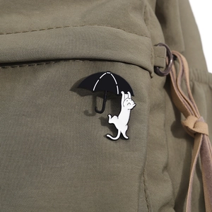 Close-up of a white cat hanging on a black umbrella enamel pin on a green canvas bag