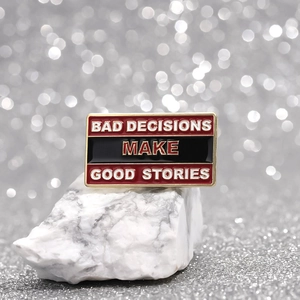 Inspirational enamel pin with BAD DECISIONS MAKE GOOD STORIES quote on a white rock