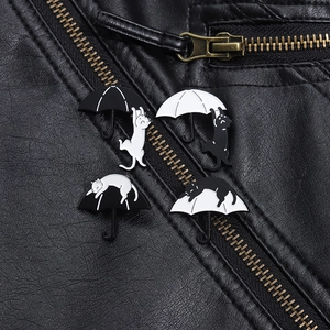 Detail von schwarz-weißen Katzen-Regenschirm-Emaille-Pins auf schwarzem Lederjacken-Stoff
