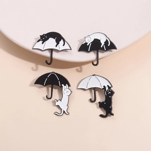Set of four black and white cartoon cat enamel pins with umbrella designs in 2x2 layout