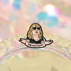 Macro detail of enamel pin with gold hair cartoon and Help Me I'm Poor pink ribbon