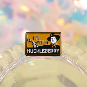 Retro cowboy metal brooch with I'm Your Huckleberry quote and gun detail on a glass rim