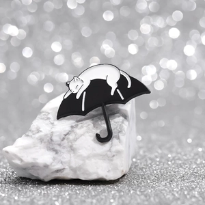 Minimalist black and white enamel pin featuring a white cat sleeping on a black umbrella