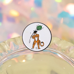 Detail of round enamel pin showing cartoon tiger playing golf with colorful bokeh background