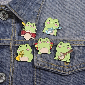 Lot de cinq pin's émaillés grenouilles musiciennes sur une veste en jean bleue