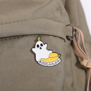 Macro shot of a cute ghost banana enamel pin with Booo-na-na text on a green backpack