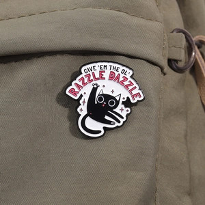 Détail d'un pin's chat noir émaillé avec lettrage blanc sur un sac en toile verte
