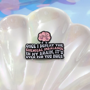 Pink cartoon brain enamel pin with funny quote on a shell-shaped display tray
