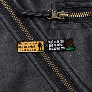 Detailed close-up of funny Bigfoot enamel pins pinned on a black leather jacket texture