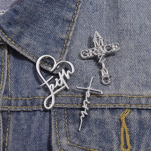 Detailed close-up of three silver metal pins with Faith and Amazing Grace on denim jacket