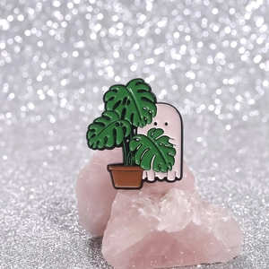 Ghost and monstera plant enamel pin on pink crystal stone with bokeh light background