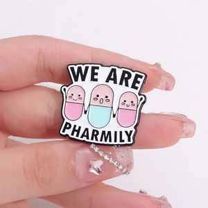 Cartoon enamel medicine pill brooches with We Are Pharmily text in hand view