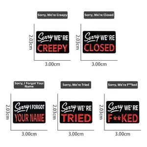 Detail view of 3.00cm x 2.03cm enamel pins with Sorry WE'RE slogans and black metal base