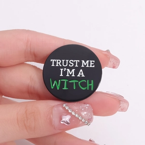Round black enamel brooch with Trust Me I'm a Witch text held in hand for size context