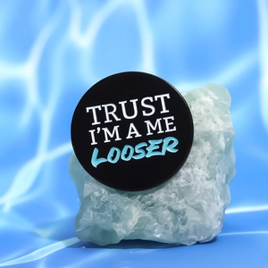 Minimalist black geometric brooch with blue TRUST ME lettering on a water ripple background