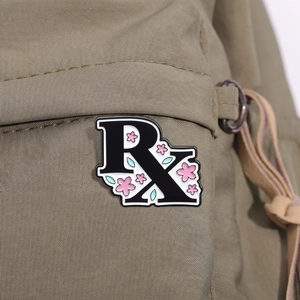 Dettaglio di una spilla smaltata RX con fiori di ciliegio rosa su borsa in nylon kaki