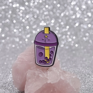Close-up of cute purple boba tea enamel pin leaning on a pink quartz stone base