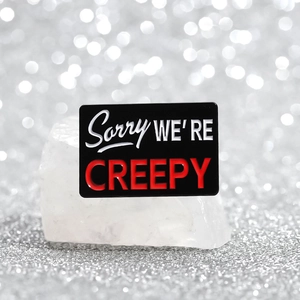 Rectangular black enamel pin with Sorry We Are Creepy text on mineral stone base