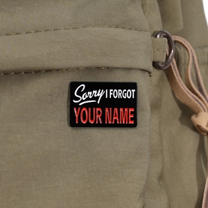 Close-up of Sorry I Forgot Your Name enamel pin on a green canvas backpack strap