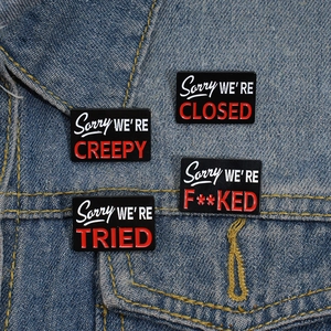 Set of four satirical enamel pins on denim jacket featuring humorous Sorry slogans