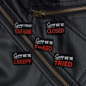 Close-up of Sorry WE'RE series enamel pins pinned on a black leather jacket detail