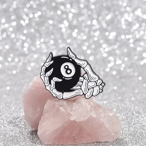 Detail einer Emaille-Brosche im Punk-Stil: Skeletthand hält eine schwarze Billardkugel 8